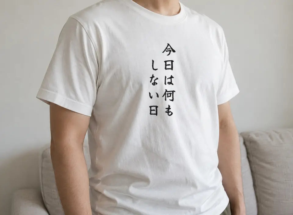 部屋で立つ人。白い T シャツの胸に、縦書きで「今日は何もしない日」。押すと、商品ページを開く