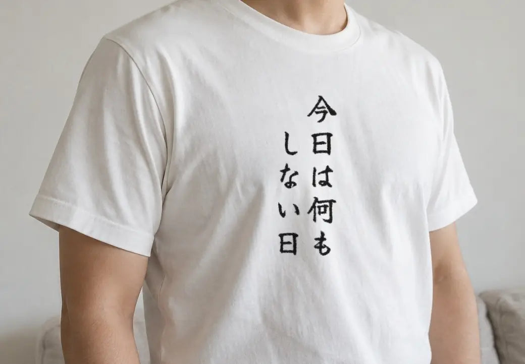 休日の昼前、リビングのソファの横に立つ人。白い T シャツの胸に縦書きで「今日は何もしない日」（画像生成の人物に、商品と同じ版下を合成）。押すと、白の商品ページを開く