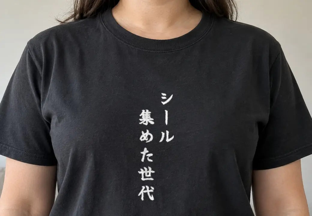 午前のリビングでソファの前に正面を向いて立つ人。黒い T シャツの胸に縦書きで「シール集めた世代」（画像生成の人物に、商品と同じ版下を合成）。押すと、黒の商品ページを開く